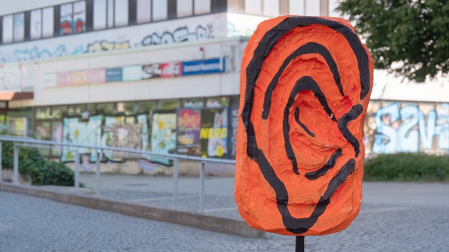 Ein orangenes plastisches Ohr steht in Grünau vor dem Stadtteilladen